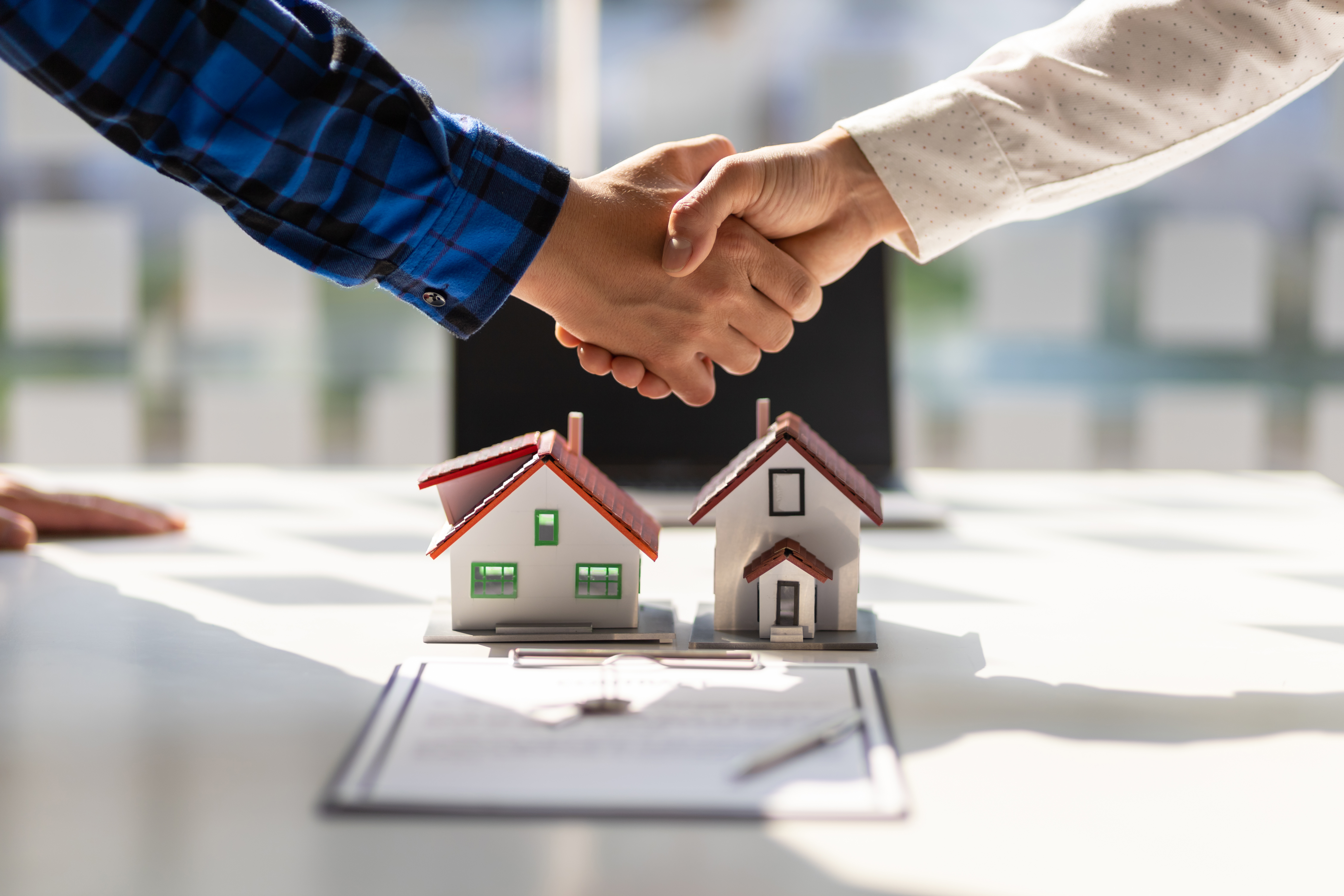 People shaking hands over two small house figurines